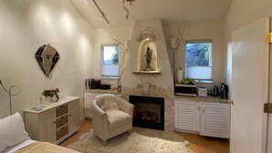 A bedroom with a fireplace, a white armchair, a dresser, and a bed. - Serene Montclair Getaway (Oakland)