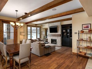 Relax in this spacious living area with a high ceiling, featuring a mounted TV, dining table, and comfortable seating.