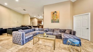 A spacious living room with a large sectional sofa, a glass coffee table, and a modern art piece on the wall. - Private House with Pool and Spa (Desert Hot Springs)
