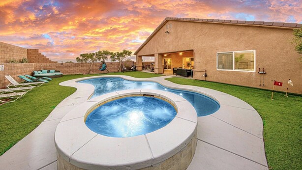 A swimming pool with a hot tub, surrounded by a patio area with lounge chairs and a building in the background. - Private House with Pool and Spa (Desert Hot Springs)