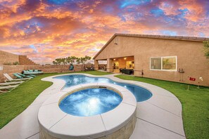A swimming pool with a hot tub, surrounded by a patio area with lounge chairs and a building in the background. - Private House with Pool and Spa (Desert Hot Springs)