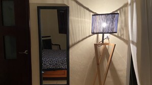 Une pièce comprenant un lit, un miroir, une lampe, une porte et une fenêtre avec des rideaux.
