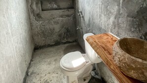Une petite salle de bain étroite, avec des toilettes blanches, un meuble-lavabo en bois et un lavabo en pierre.
