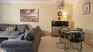 Un salon moderne avec un canapé gris, une table à manger avec des chaises, un coin cuisine et un tableau encadré au mur.