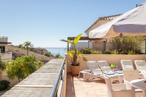 Un balcón con vista al mar, sillones blancos para relajarse y una planta en maceta.