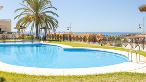 Une piscine avec un palmier, un poste de surveillance pour les sauveteurs et une vue sur la mer.