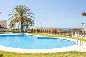 Une piscine avec un palmier, un poste de surveillance pour les sauveteurs et une vue sur la mer.