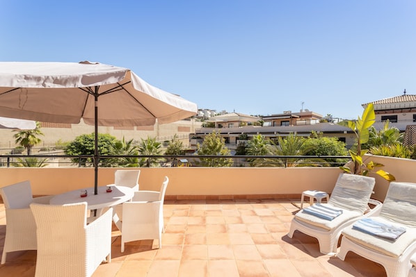 Une terrasse dotée de meubles en osier blanc, d’une table et d’un parasol.