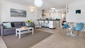 A modern living room with a sofa, coffee table, and a dining area with chairs and a table.