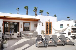 Une terrasse ensoleillée, aménagée avec du mobilier d’extérieur, un hamac et des palmiers.