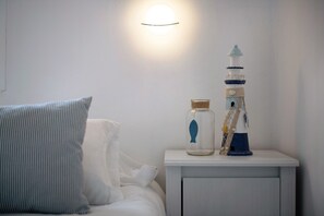Un lit avec un oreiller à rayures, une table de chevet ornée d’une maquette de phare et d’un bocal en forme de poisson, et une lampe fixée au mur.