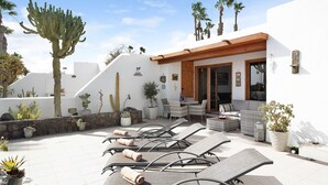 A patio with sun loungers, a stone wall, and potted plants.