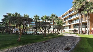 A courtyard with cobblestone paths, palm trees, and a multi-story building with balconies. - Salgados 4Seasons Apartment with Pool, A/C, Wi-Fi, Garden & Balcony (Albufeira)