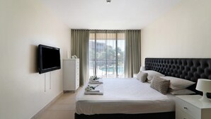 A hotel room with a bed, a TV, a nightstand, and a view of a pool. - Salgados 4Seasons Apartment with Pool, A/C, Wi-Fi, Garden & Balcony (Albufeira)