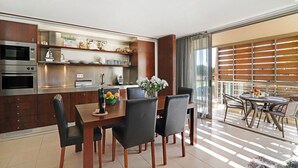 A modern kitchen with built-in appliances, a dining area with a wooden table and chairs, and a balcony with a view. - Salgados 4Seasons Apartment with Pool, A/C, Wi-Fi, Garden & Balcony (Albufeira)