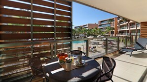 A balcony with a table set for breakfast, a chair, and a view of a pool and buildings. - Salgados 4Seasons Apartment with Pool, A/C, Wi-Fi, Garden & Balcony (Albufeira)
