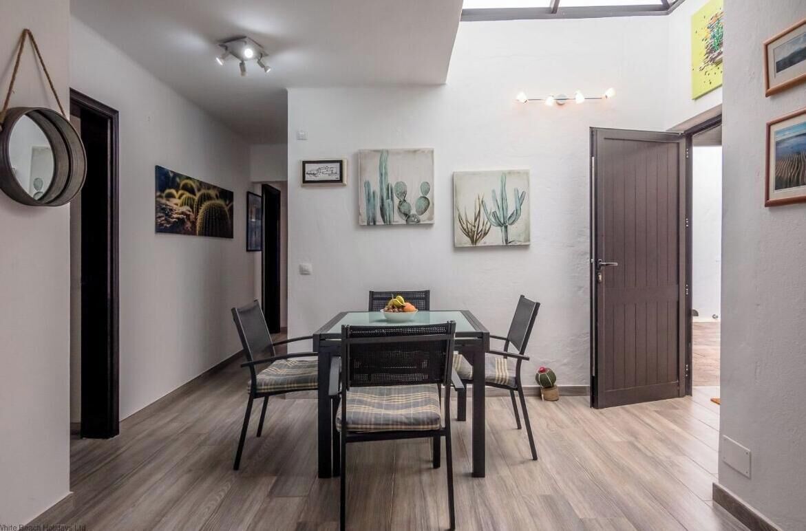A dining area with a glass-top table, four chairs, and cactus-themed artwork on the walls.