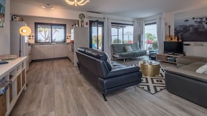 A modern living room with a sofa, a coffee table, a TV, and a dining area with a lamp.
