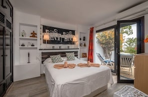 A bedroom with a bed, a nightstand, a wall-mounted lamp, a window with curtains, and a view of the outdoors.