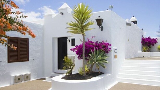 A white building with a door, a small garden with plants, and a staircase.