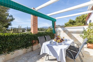 Une terrasse avec une table dressée pour le petit-déjeuner, entourée de chaises, d’un auvent vert et offrant une vue sur le paysage.