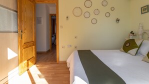 Un dormitori amb un llit, una porta de fusta, elements decoratius penjats a la paret i un passadís.
