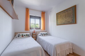 Quarto com duas camas, janela com cortinas, mesa de cabeceira com abajur e um quadro na parede.