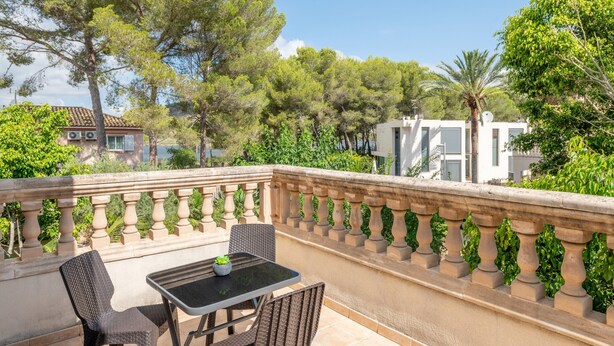A balcony with a table and chairs, surrounded by greenery and buildings.