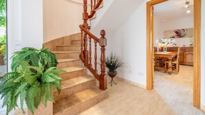 A staircase with wooden balusters, a dining area with a wooden table and chairs, and a potted plant.