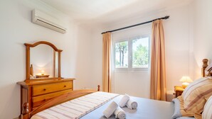 A bedroom with a bed, a dresser, a mirror, a window with curtains, and a lamp.