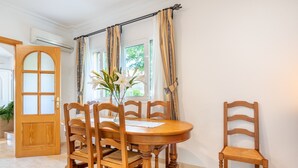 A dining area with a wooden table and chairs, a vase with flowers, and a window with curtains.