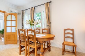 Un coin repas avec une table et des chaises en bois, un vase rempli de fleurs et une fenĂȘtre avec des rideaux.