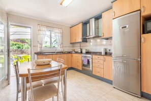 A modern kitchen with wooden cabinets, a stainless steel refrigerator, and a dining table with chairs.