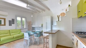 A modern kitchen with a gas stove, white cabinets, and a dining area with a green sofa and a table.