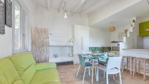 A modern, well-lit room with a bunk bed, a dining table with chairs, and a kitchen area.