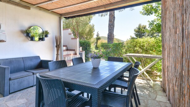 An outdoor patio with a table, chairs, a sofa, and potted plants.