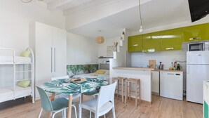 A modern kitchen with white cabinets, a green accent wall, a dining area with a table and chairs, and a built-in oven.