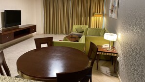 Un salon avec une table de salle à manger ronde, un téléviseur posé sur un meuble en bois, un canapé et une lampe.