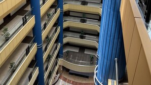 Un atrium à plusieurs niveaux, doté d’un espace central ouvert, entouré de balcons avec des garde-corps et des plantes en pot.