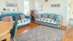 A living room with two sofas, a wooden dining table, a rug, and a bookshelf. - Lake, mountain view cottage - Entire house (Rotorua)