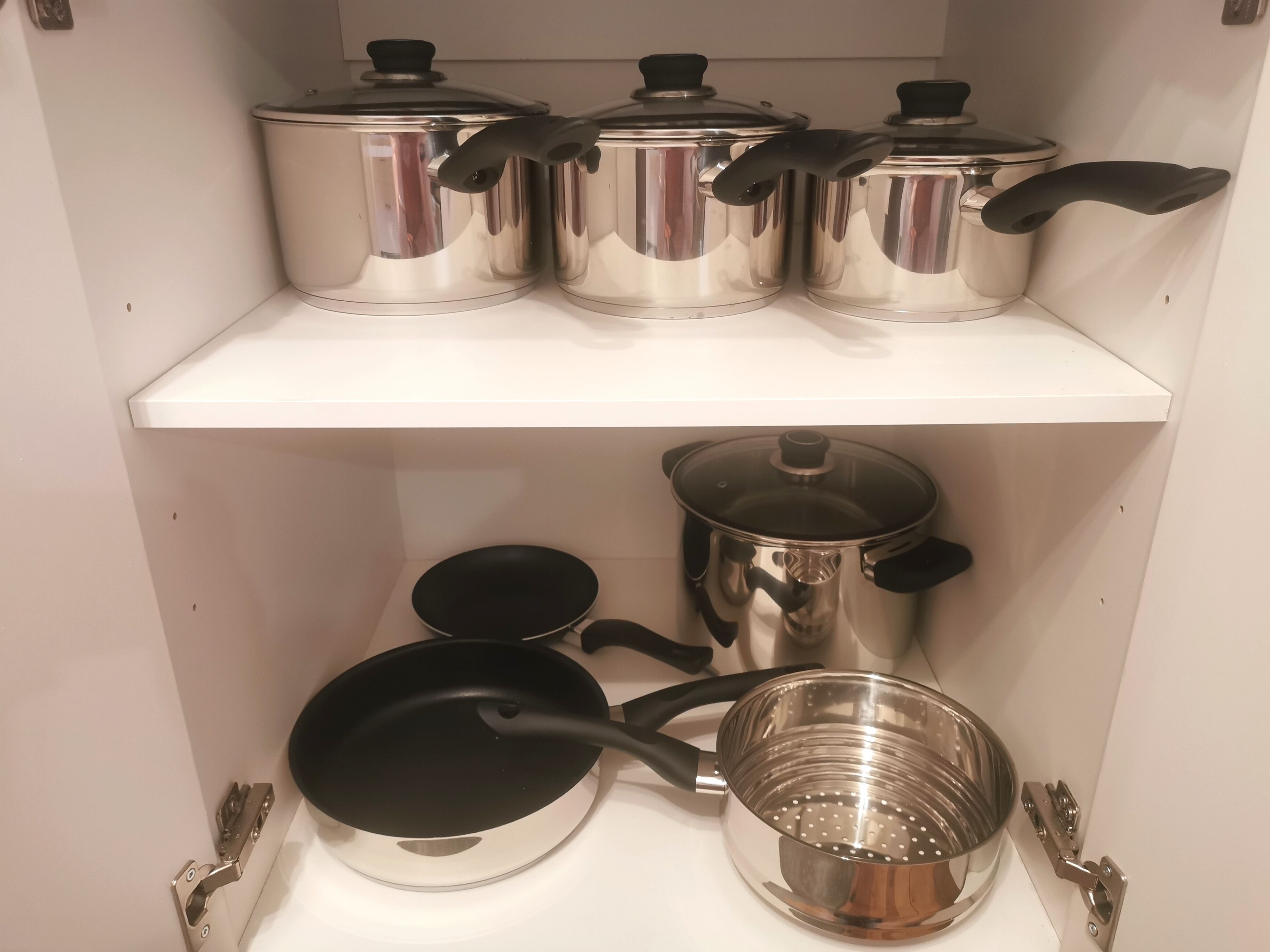 A kitchen with stainless steel cookware on shelves, including pots, pans, and a colander.