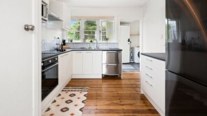 A modern kitchen with white cabinets, stainless steel appliances, and a wooden floor. - Lake, mountain view cottage - Entire house (Rotorua)