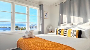 A hotel room with a bed, a window with a view of the sea, and a fan on the nightstand. - Lake, mountain view cottage - Entire house (Rotorua)