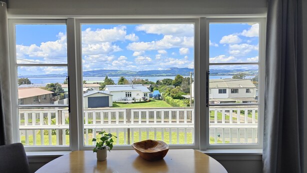 A room with a view of a residential area, a wooden table, and a potted plant. - Lake, mountain view cottage - Entire house (Rotorua)