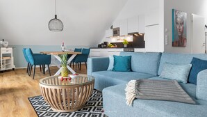 Una sala de estar moderna con un sofá azul, una mesa de centro redonda y una zona de comedor con mesa y sillas de madera.