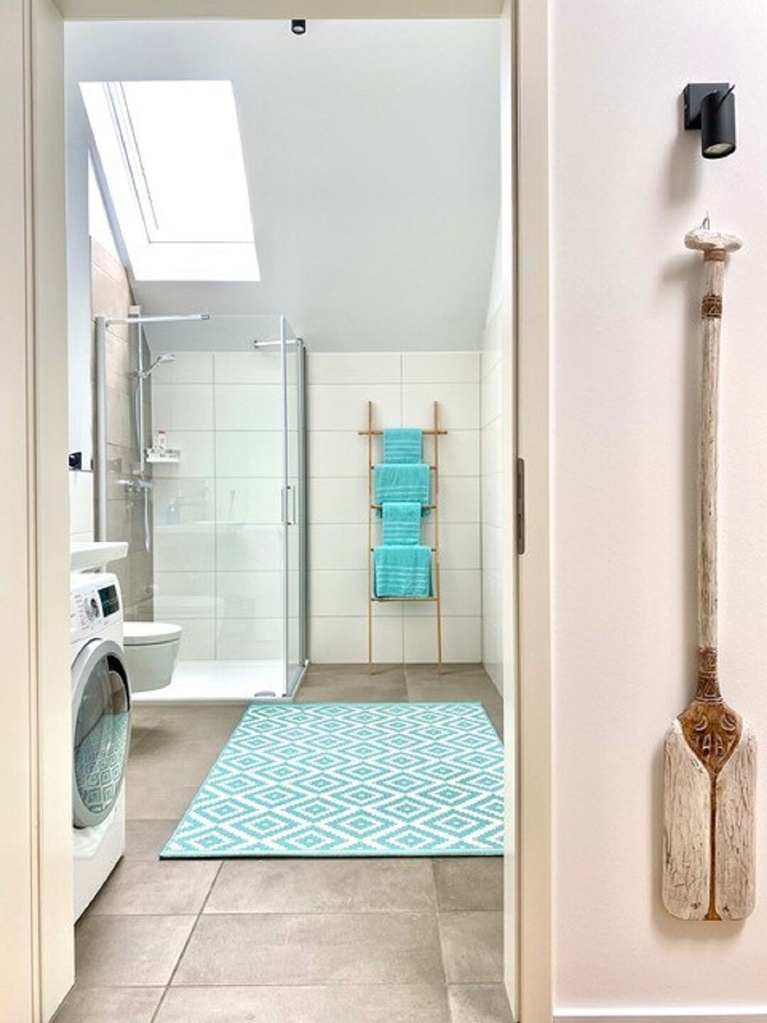 A modern bathroom with a glass shower enclosure, a washing machine, and a blue patterned rug.