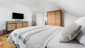 Un dormitorio con techo inclinado, una cama con manta a rayas, un armario de madera y un televisor en la pared.