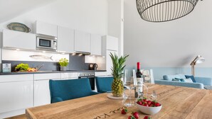 Una cocina moderna con armarios blancos, un microondas y una cafetera. Hay una mesa de madera con un tazón de fresas y una piña.