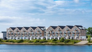 A row of modern multi-story buildings with balconies, situated by a body of water.