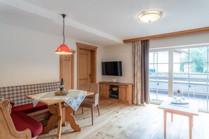 A cozy room with a wooden table, a sofa, a TV, and a large window.